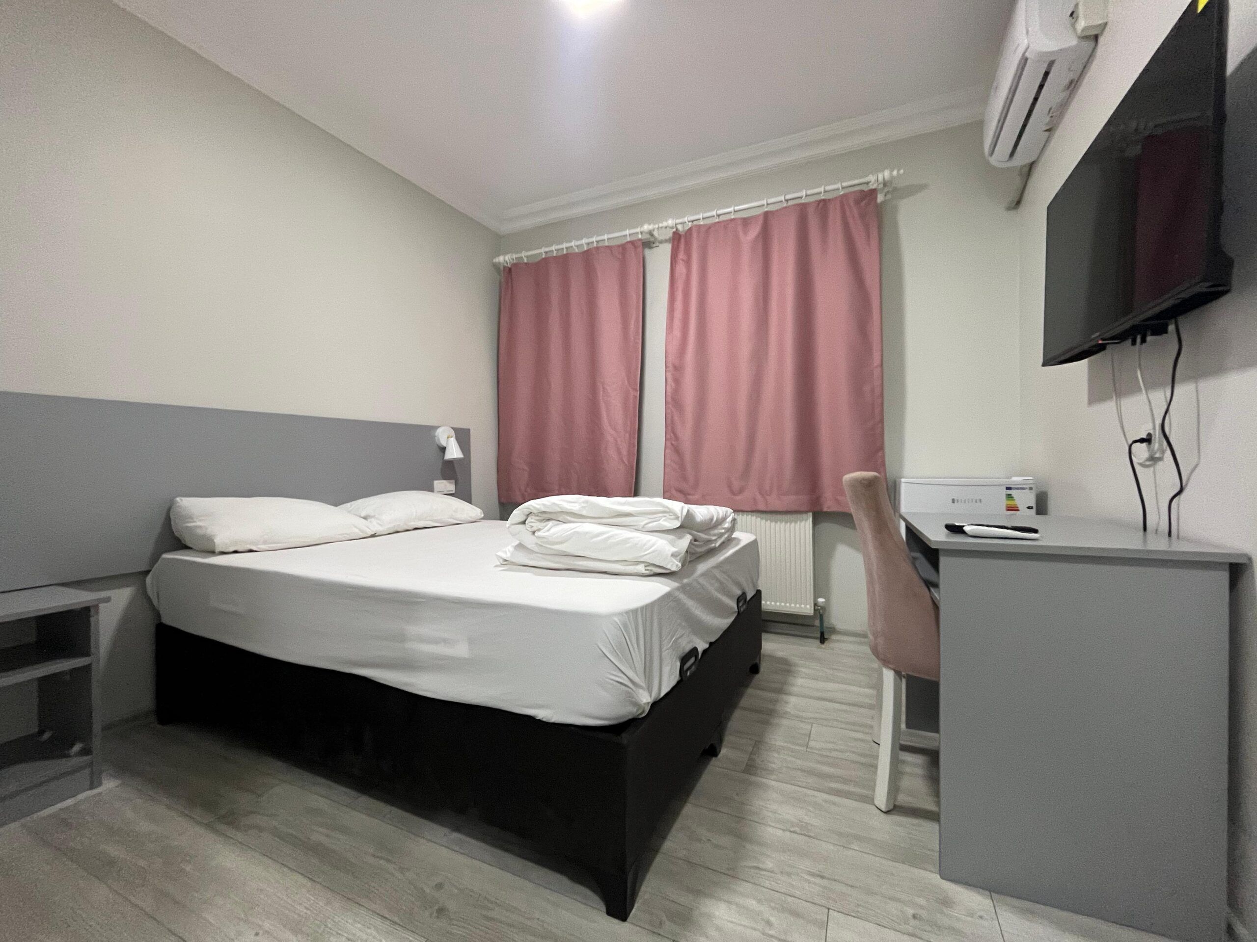 A hotel room with a bed, a desk, a chair, a TV, and a window with curtains.
