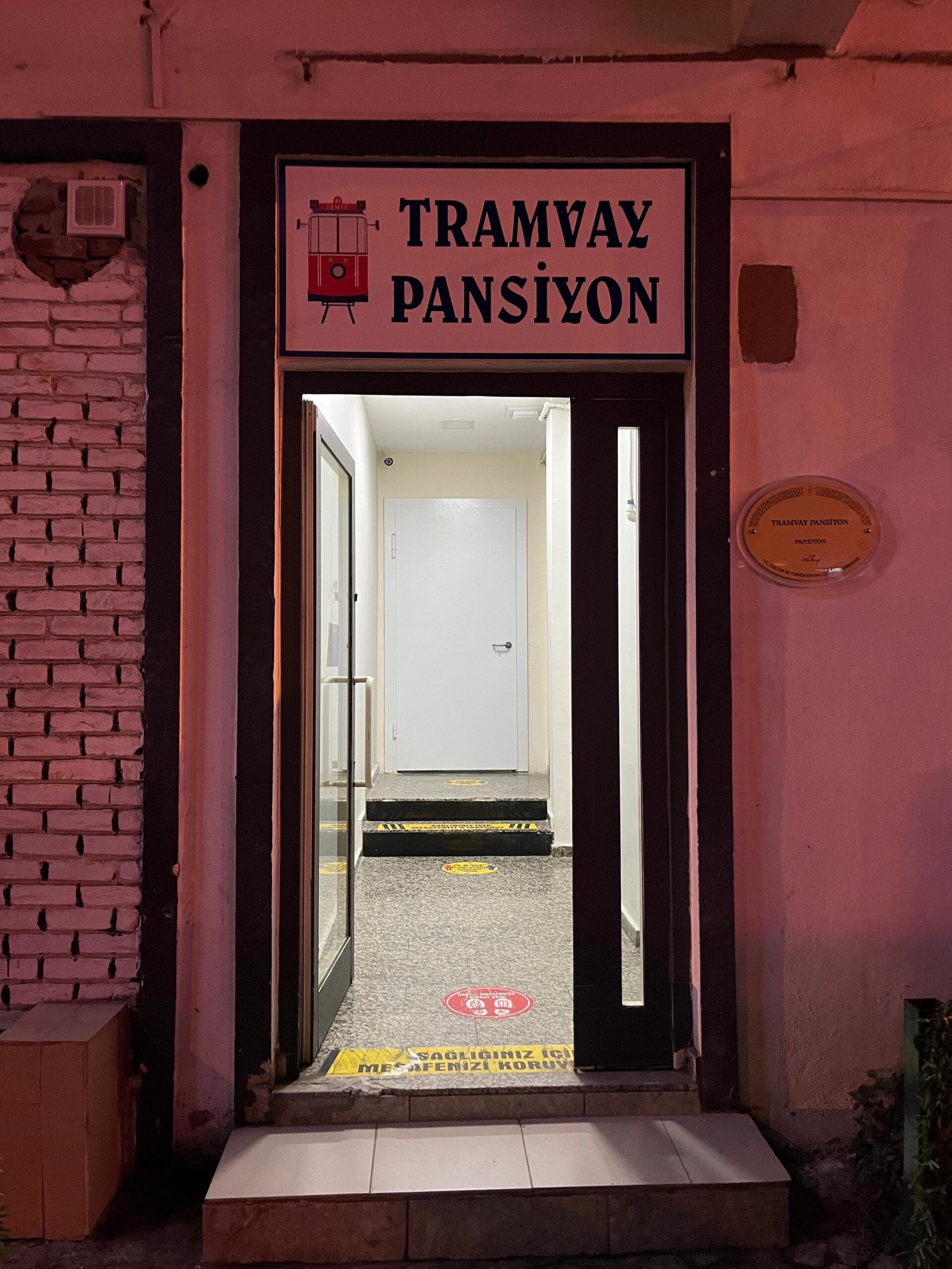 En byggnadsentré med en skylt som visar texten ”TRAMVAY PANSIYON” och en plakett under skylten.