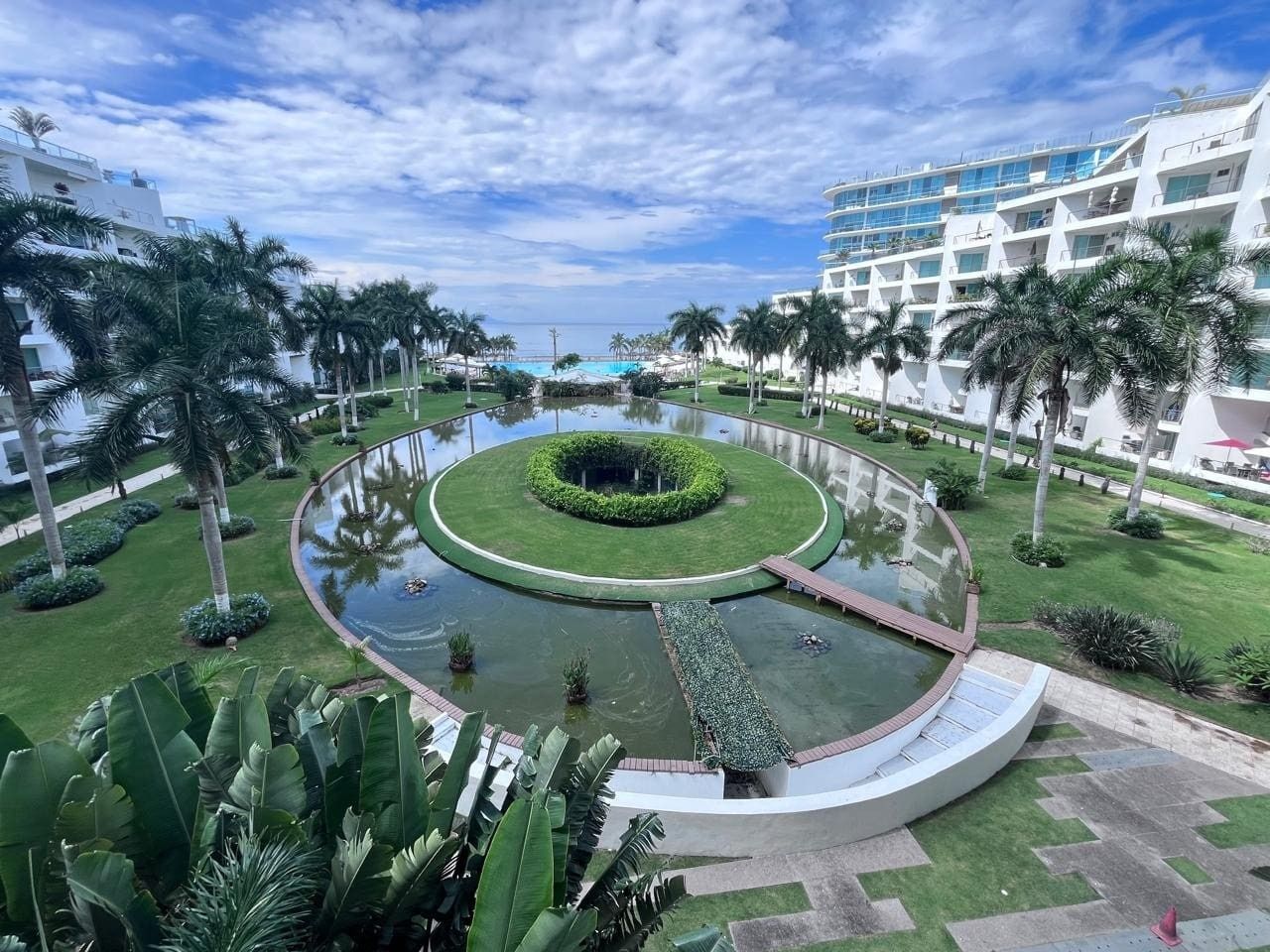 Un hôtel doté d’un bassin circulaire, de palmiers et d’une piscine.