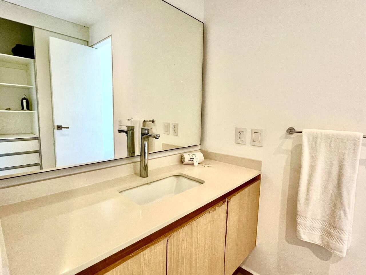 A bathroom with a white sink, a mirror, a towel hanging on a rack, and a wooden cabinet.