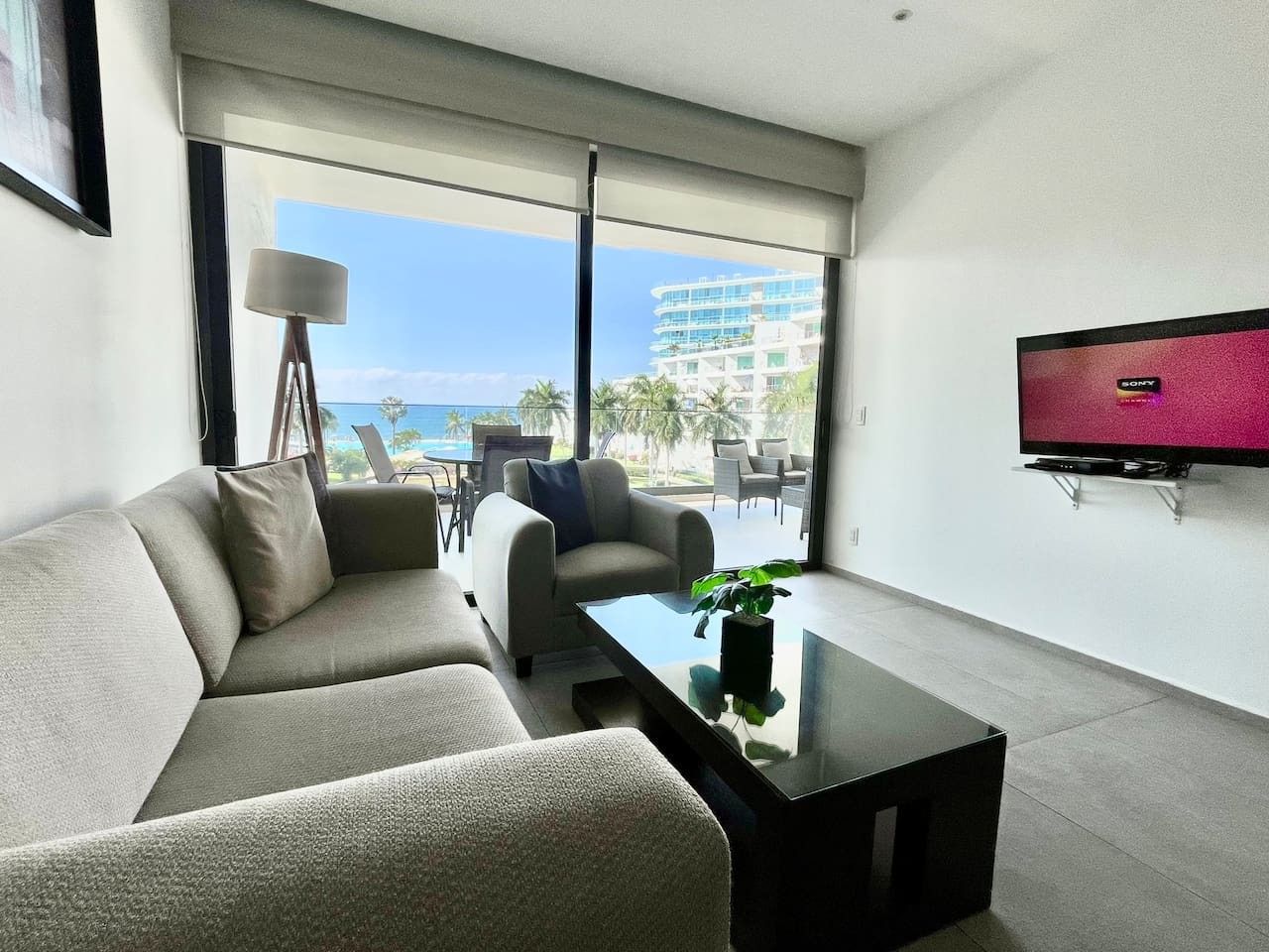 A modern living room with a sofa, armchair, and coffee table. A flat-screen TV is mounted on the wall.