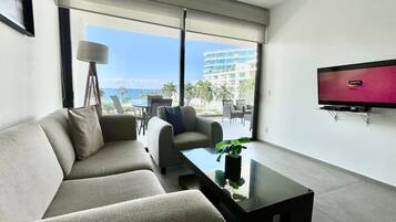 A modern living room with a sofa, armchair, and coffee table. A flat-screen TV is mounted on the wall.