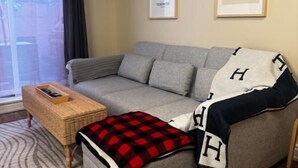 A living room with a grey sofa, a small ottoman, a wicker side table, and a framed picture on the wall.