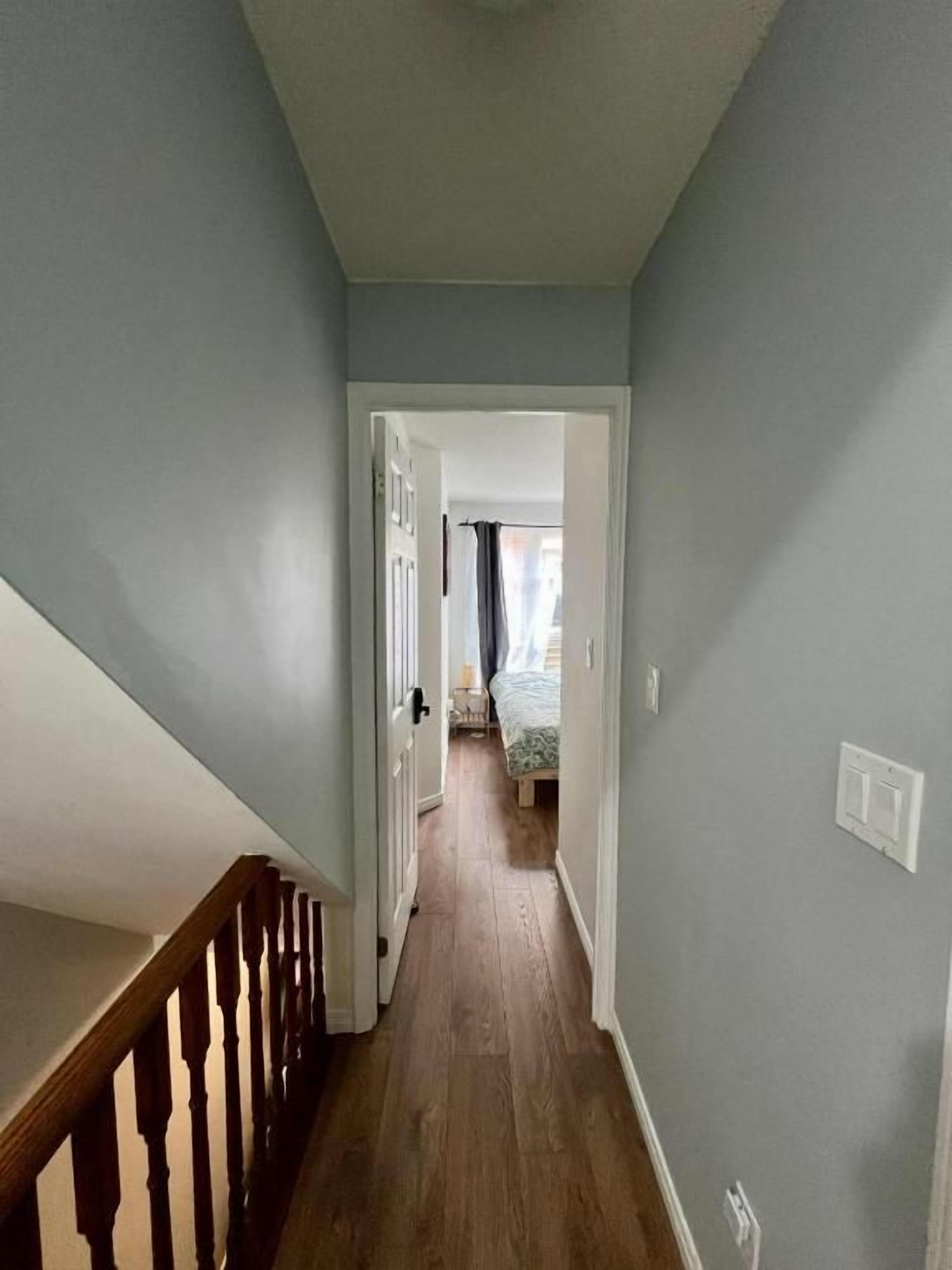 Um corredor com guarda-corpo de madeira, uma porta que dá para um quarto e um interruptor de luz na parede.