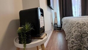 A hotel room with a bed, a small table with a coffee machine, a potted plant, and a TV mounted on the wall.