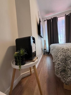 A hotel room with a bed, a small table with a coffee machine, a potted plant, and a TV mounted on the wall. - DT Townhouse Room Steps to Transit (Toronto)