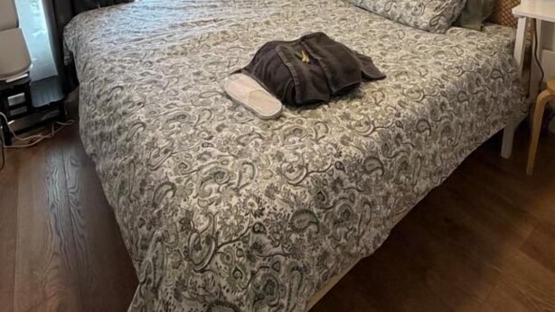 A bedroom with a double bed, a nightstand, a lamp, a painting, and a window with curtains.