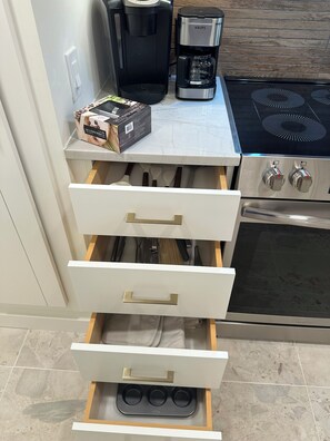 Eine Küche mit Kaffeemaschine, einer Kapselbox und einer Schublade voller Besteck.