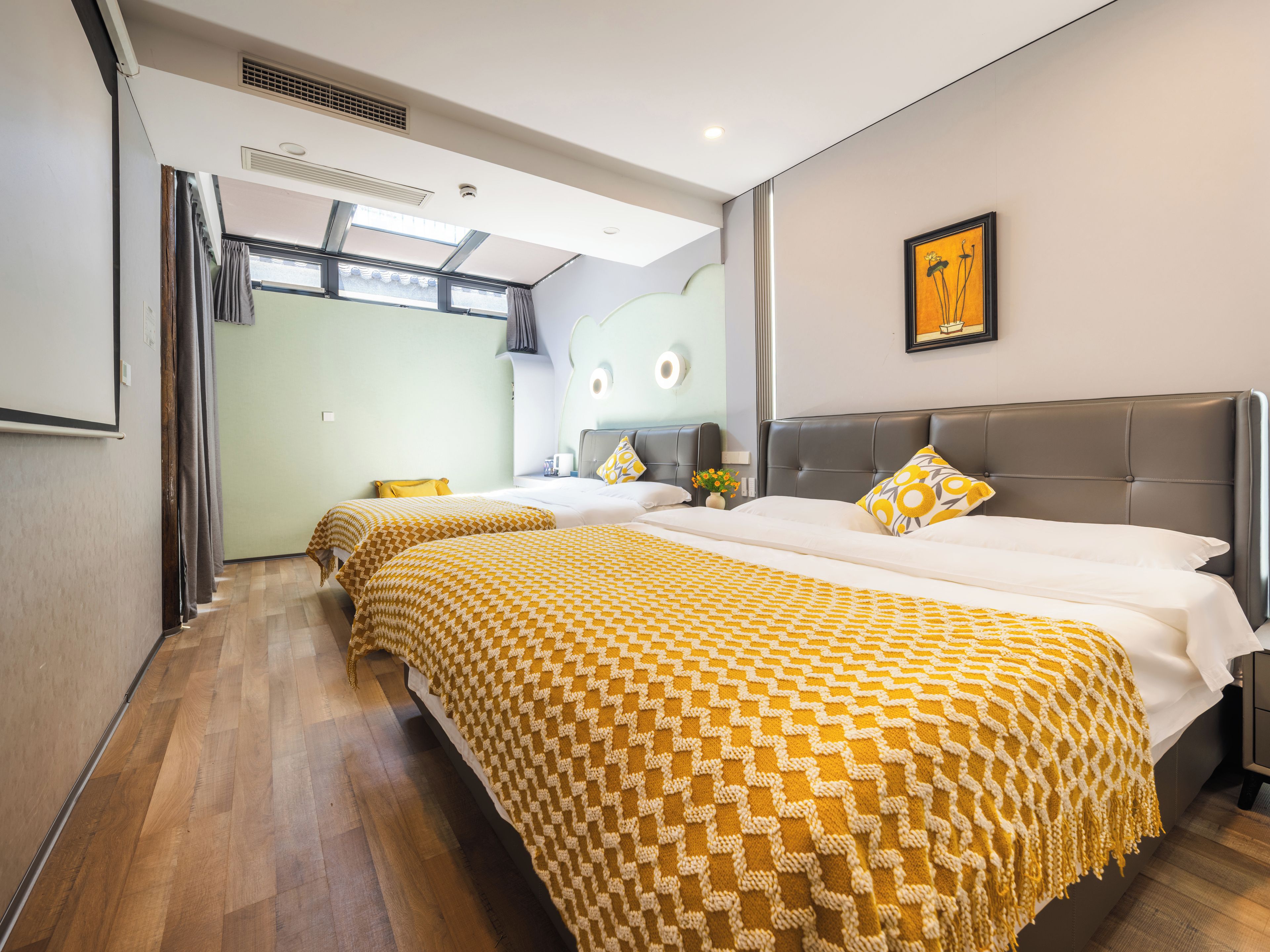 A hotel room with two beds, a large window, a wall-mounted artwork, and a ceiling vent.