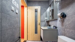 A modern bathroom with a wooden door, a white toilet, a sink with a mirror, and a hairdryer mounted on the wall. - Harbor City (Universal Beijing Resort) (Tongzhou District, Beijing)