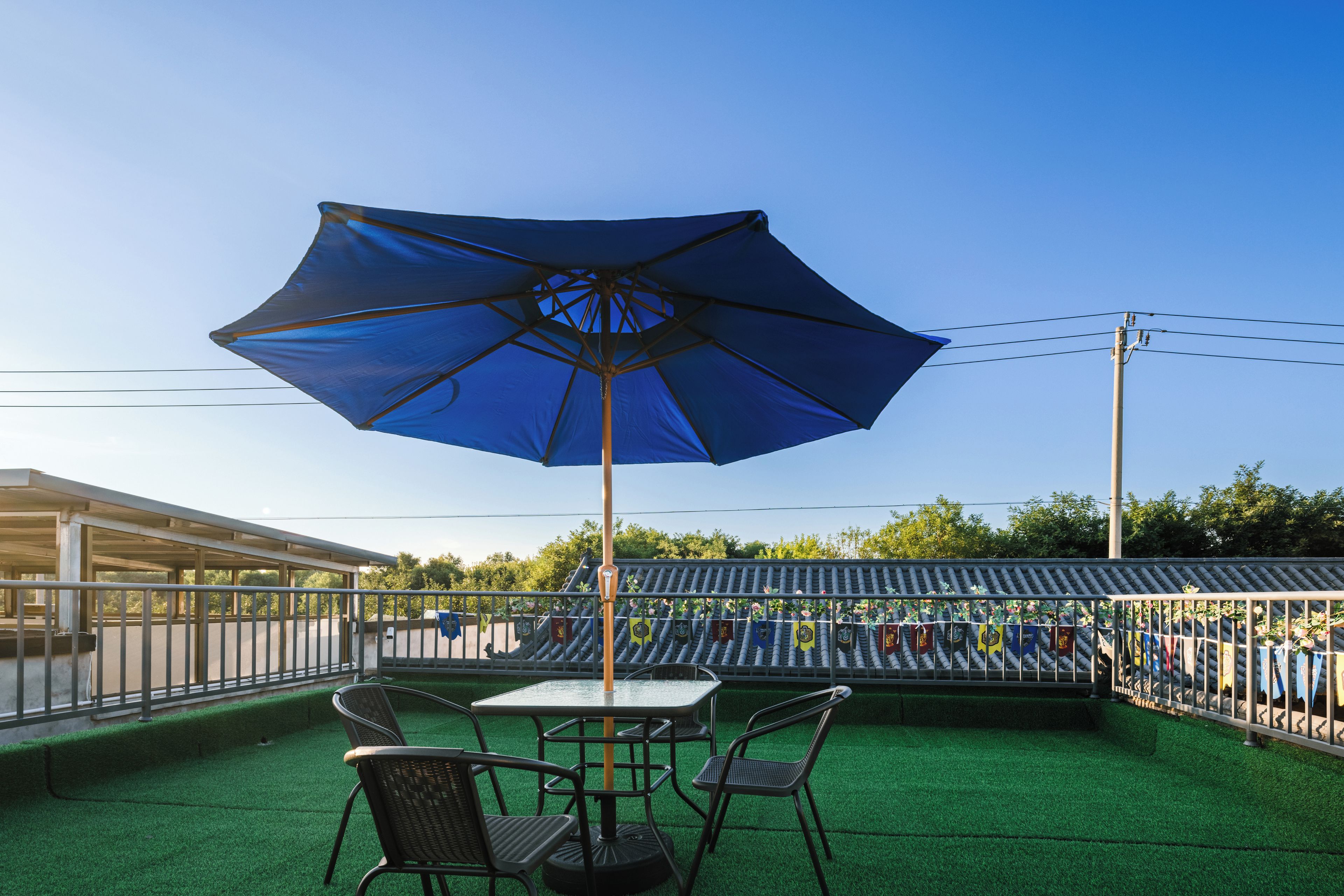 An outdoor seating area with a table and chairs under a blue umbrella, surrounded by a railing with flags.