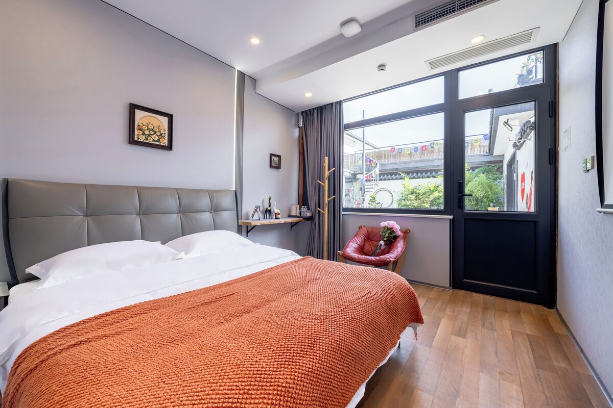 A modern hotel room with a large bed, a window with a view of the outside, a small desk, and a chair.