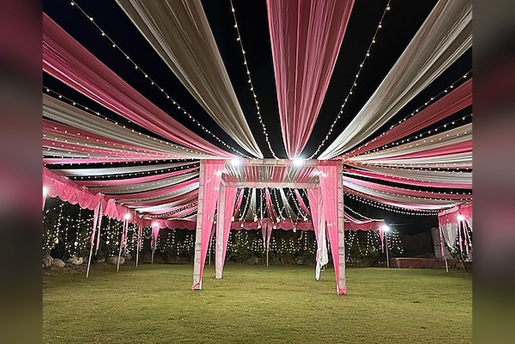 An outdoor event space with a tent structure, string lights, and a grassy area.