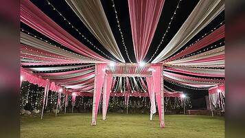 An outdoor event space with a tent structure, string lights, and a grassy area.