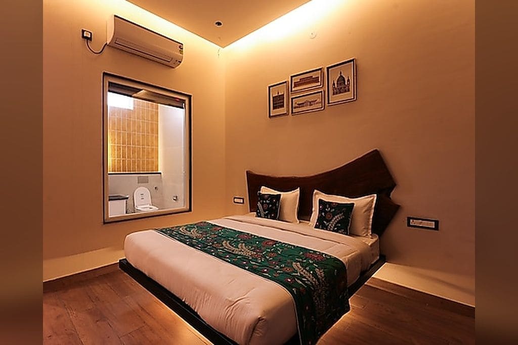 A hotel room with a bed, a large window, and a wall-mounted air conditioner.