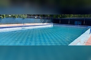 A swimming pool with a checkered pattern on the floor, surrounded by a fence and a covered area.