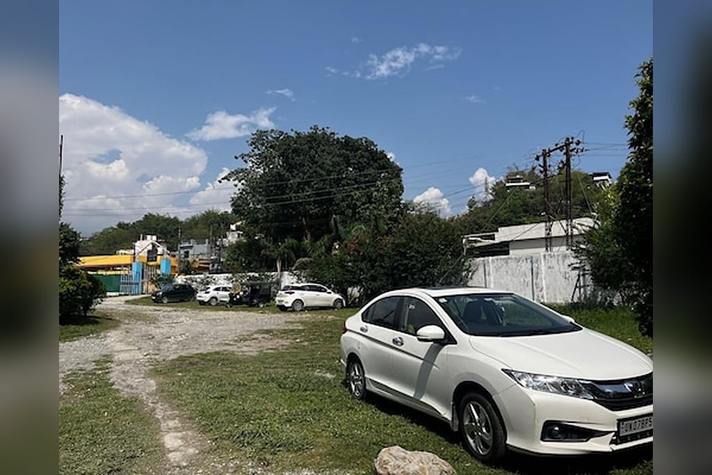 A white car parked on a grassy area with buildings and trees in the background.