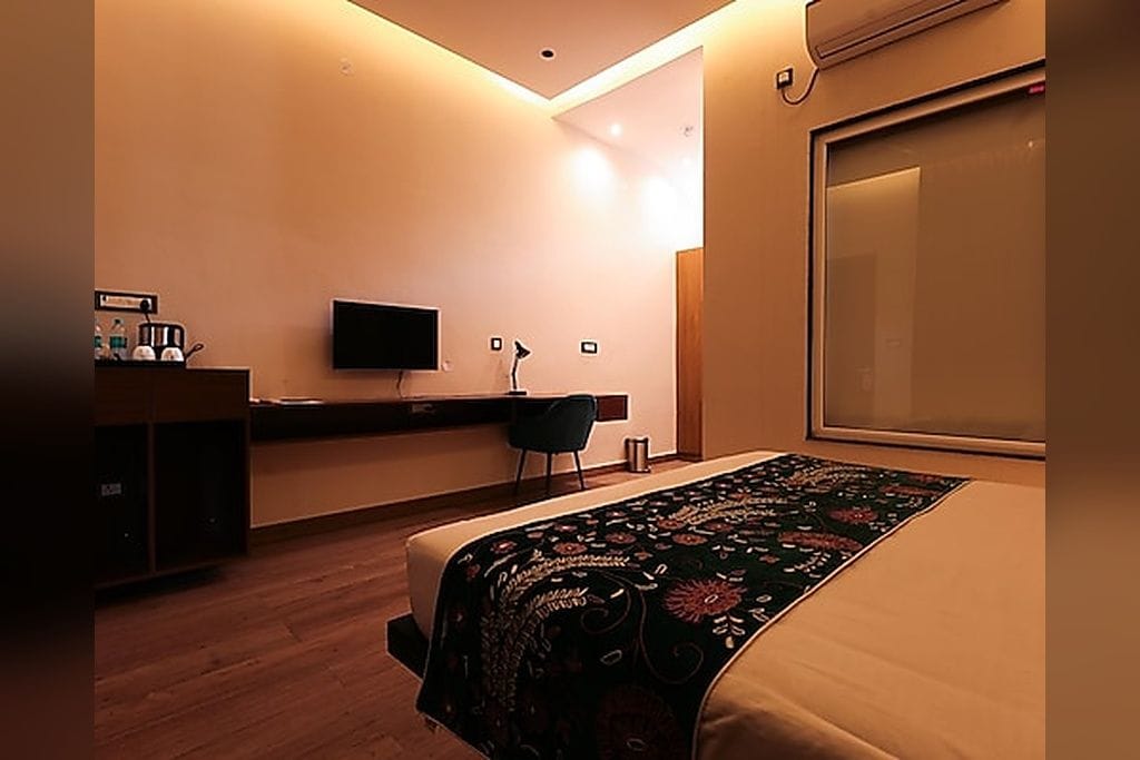 Una habitación de hotel con una cama, un escritorio, un televisor y un ventanal grande.