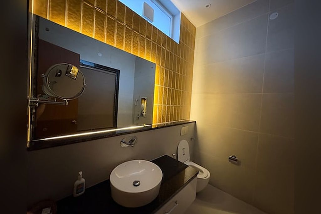 Un baño moderno con un espejo grande, un lavabo redondo y un inodoro.