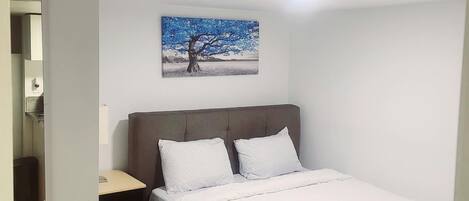 A bedroom with a bed, a nightstand, a drawer, a painting on the wall, and a ceiling light.
