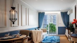 Comedor con mesa dispuesta para dos, sofá y vista al exterior a través de una ventana.