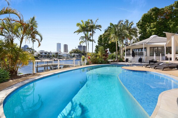 A swimming pool with a view of a marina and city skyline, surrounded by palm trees and lounge chairs. - Tranquil Waterfront Retreat Broadbeach Waters (Gold Coast)