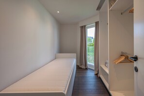 A minimalist room with a single bed, a door with a coat rack, and a window with curtains. - Elegant Apartment Near Casino (Knokke-Heist)