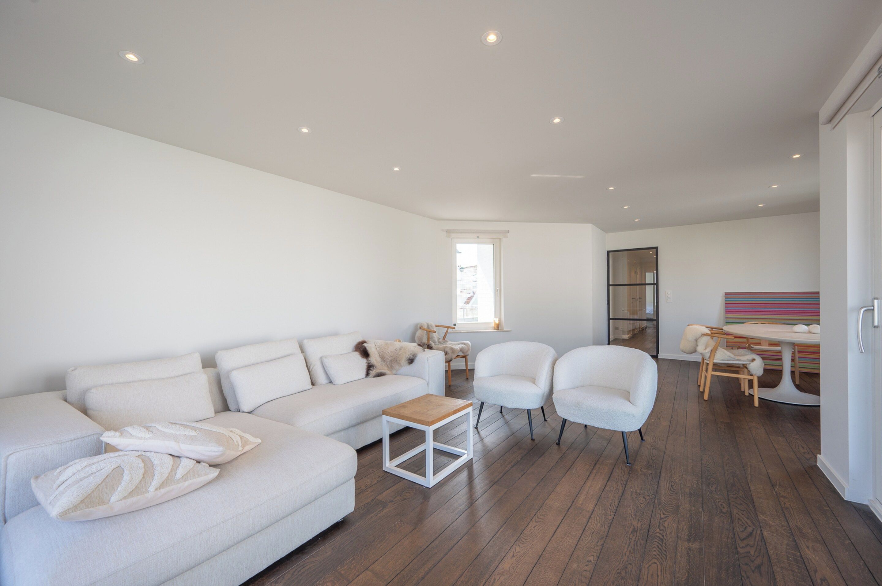 Ein modernes Wohnzimmer mit einer Couch, Sesseln, einem Couchtisch und einem Essbereich mit Tisch und Stühlen.