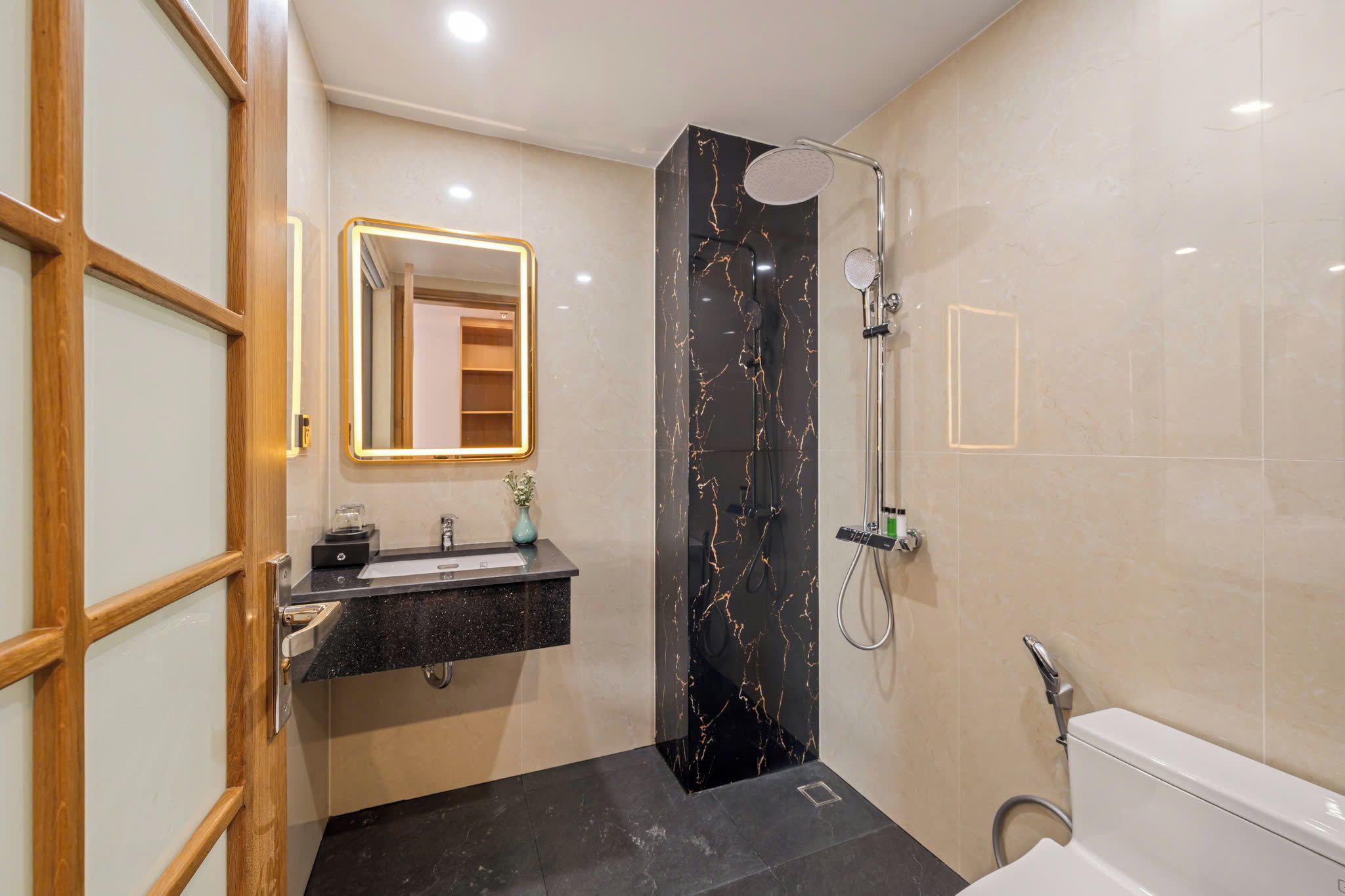 A modern bathroom with a black marble shower, a sink with a mirror, and a toilet.