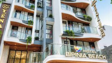 Et hotel med flere etager, altaner, en markant indgang og et skilt med teksten 'BIPINIA BEACH HOTEL'.