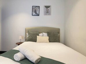 A neatly made bed with pillows and a rolled towel, a bedside lamp, and two framed artworks on the wall. - Modern 1BR - Exposed Brick - Gym - Monthly Stay (Manchester)