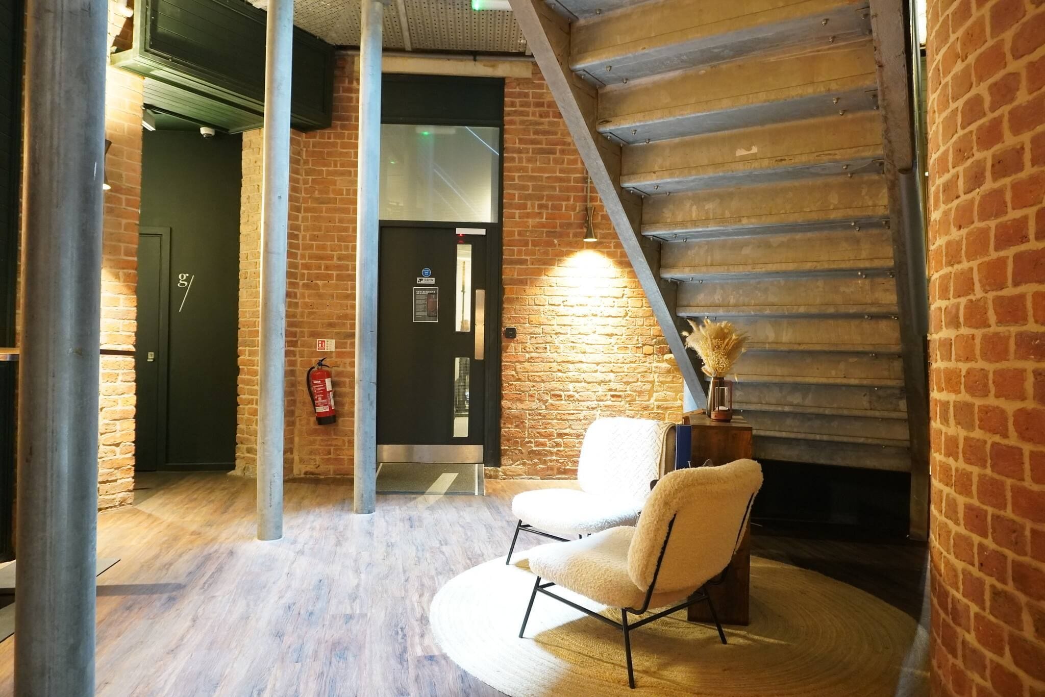 Una habitación con pared de ladrillo, escalera, una silla blanca y extintor.