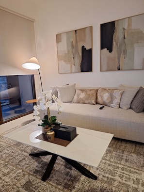 A modern living room with a sofa, a coffee table with a plant, abstract art on the wall, and a lamp.