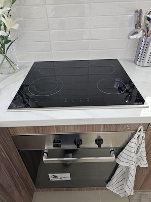 A kitchen with a black induction cooktop, a stainless steel oven, and a wooden cabinet below.