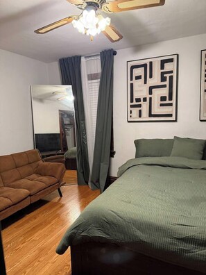 A bedroom with a bed, a sofa, a ceiling fan, and a mirror. - Historic STL Home near Wash U/Massive Backyard (University City)