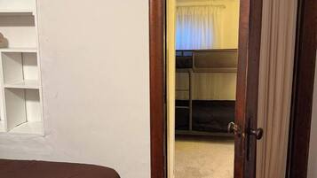 Ein Schlafzimmer mit einem Bett, einer Holztür, einem weißen Regal und Blick in einen angrenzenden Raum mit Bett und Vorhängen.