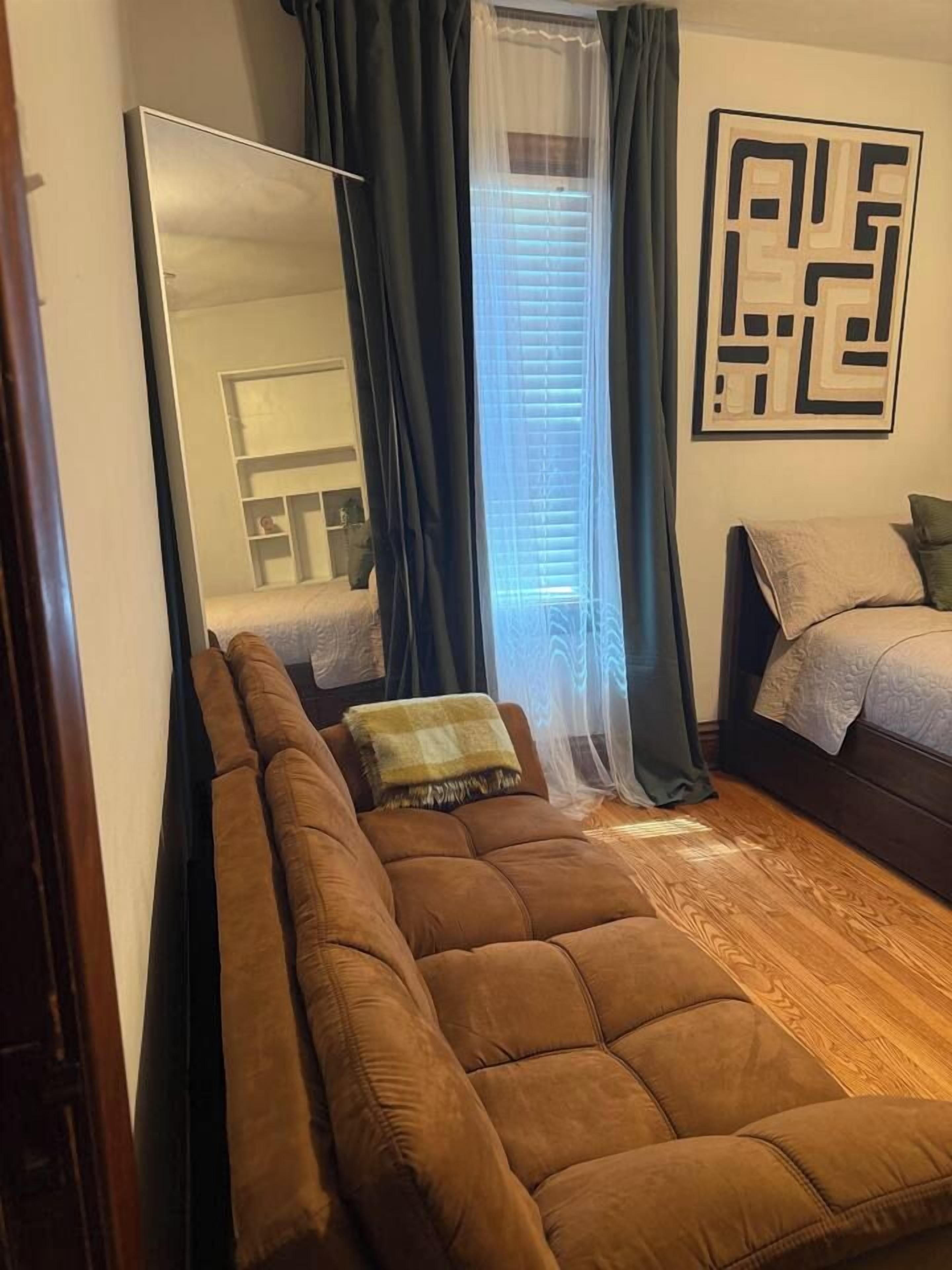 Un dormitorio con una cama grande, un sofá, un espejo y una ventana con cortinas.