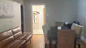 A living room with a brown leather sofa, a dining table with chairs, and a Wi-Fi sign. - Historic STL Home near Wash U/Massive Backyard (University City)