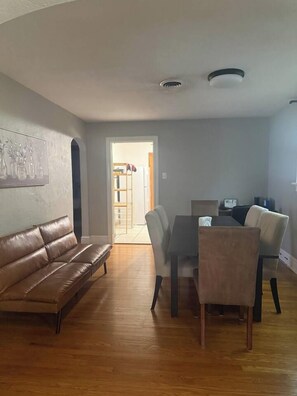 A living room with a brown leather sofa, a dining table with chairs, and a Wi-Fi sign. - Historic STL Home near Wash U/Massive Backyard (University City)
