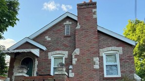 A two-story brick house with a chimney, a front door, and a small porch. - Historic STL Home near Wash U/Massive Backyard (University City)
