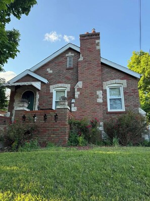 A two-story brick house with a chimney, a front door, and a small porch. - Historic STL Home near Wash U/Massive Backyard (University City)
