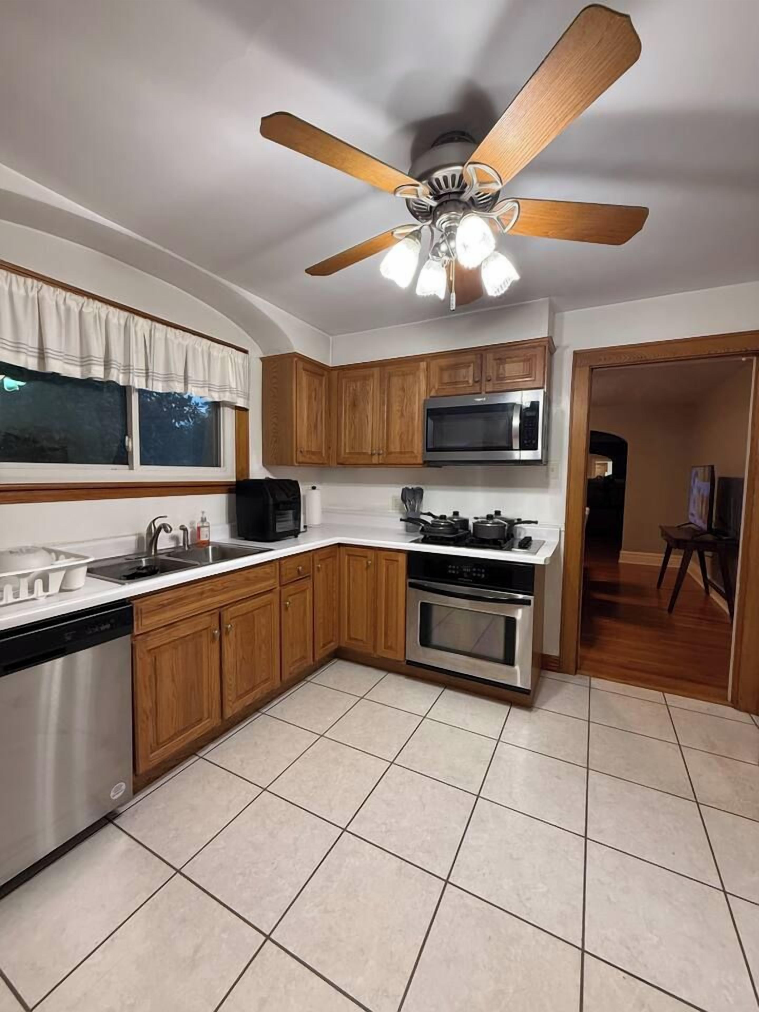 Una cocina con gabinetes de madera, microondas, horno, lavavajillas y ventilador de techo.