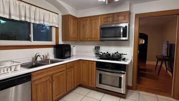 Una cocina con gabinetes de madera, microondas, horno, lavavajillas y ventilador de techo.