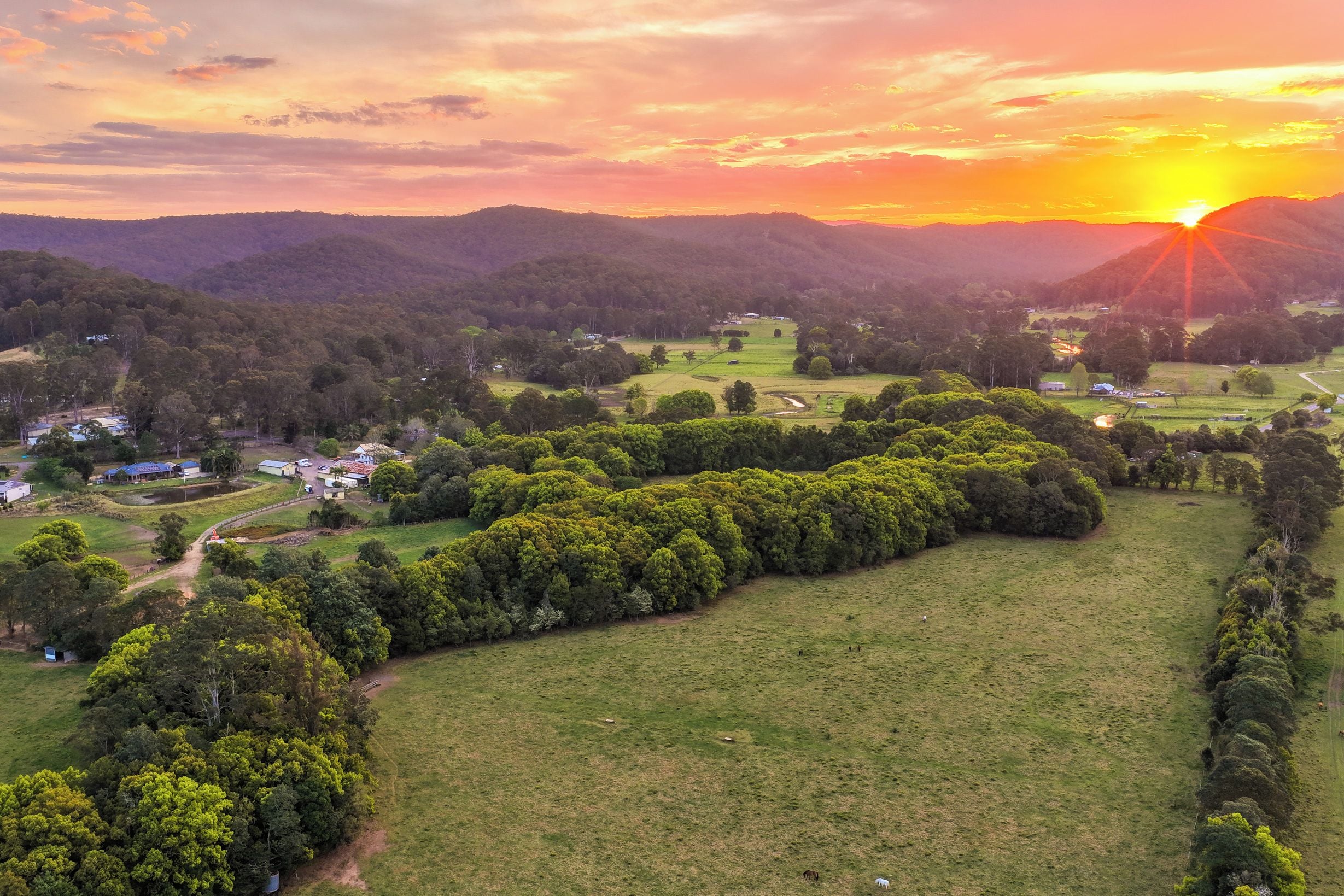 A rural landscape with a sunset, green fields, and scattered buildings.