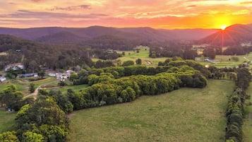 A rural landscape with a sunset, green fields, and scattered buildings.