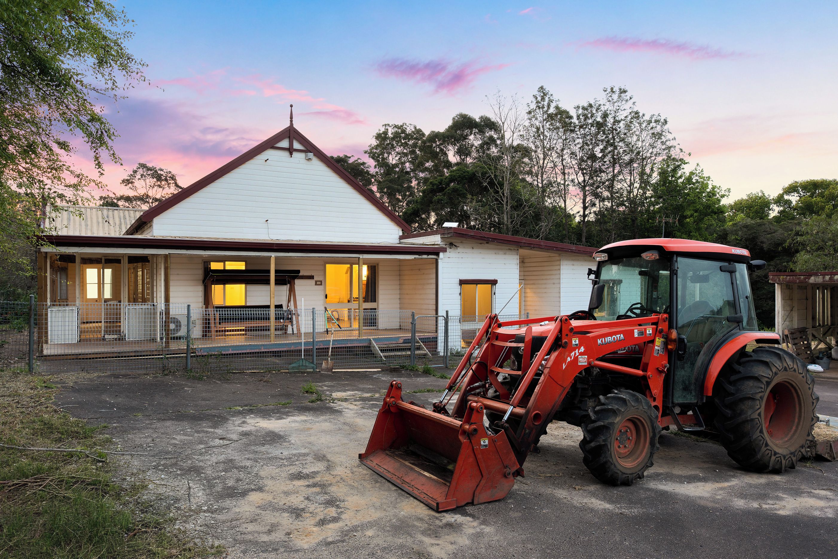 Un edificio con porche y un tractor Kubota rojo estacionado al frente.