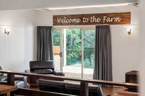 A room with a 'Welcome to the Farm' sign, a sofa, a table, and a view of greenery outside.