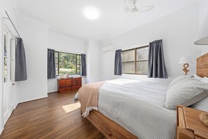 Un dormitorio con una cama de madera, una mesita de noche, un aparador y dos ventanas con cortinas.