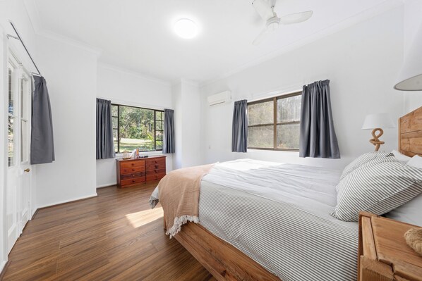 A bedroom with a wooden bed, a nightstand, a dresser, and two windows with curtains.