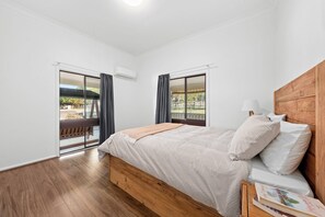 A bedroom with a wooden bed, a nightstand, a lamp, and a view of the outdoors through a sliding door.